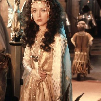 Cheri Lunghi as Guinevere in John Boorman's "Excalibur" embodies the tragic queen of Arthurian legend. Woman in golden medieval dress with ornate headpiece standing in candlelit castle interior from 1981 film.